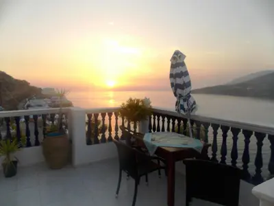 a balcony with a table and an umbrella and the sunset at Annas Studios in Livadia