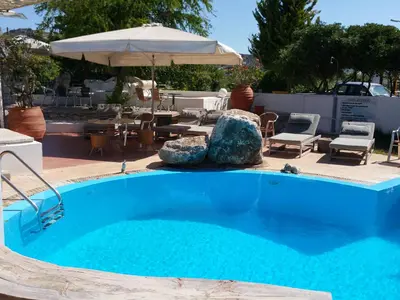 a blue swimming pool with chairs and an umbrella at Gorgona Studios in Faliraki