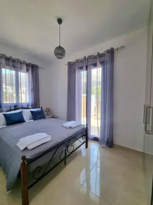 a bedroom with a bed with blue sheets and windows at Dionysia apartments in Livadia