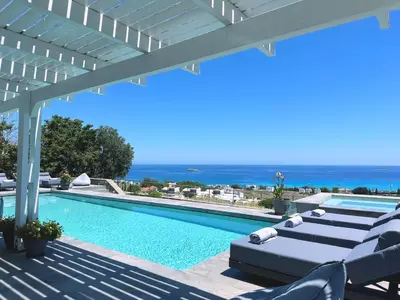 a swimming pool with lounge chairs and the ocean at Solis Lindos Villa in Líndos