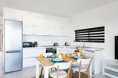 a white kitchen with a wooden table and chairs at Aquarama Pool Apt. - Blue in Ixia