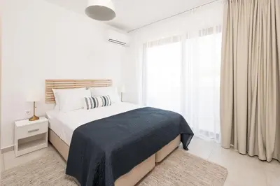 a white bedroom with a bed and a large window at Aquarama Pool Apt. - Blue in Ixia