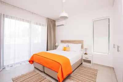 a white bedroom with a bed with an orange blanket at Aquarama Pool Apt. - Blue in Ixia