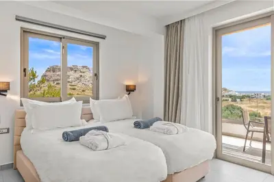 two beds in a hotel room with a large window at KOUROS STONE SUITES in Haraki