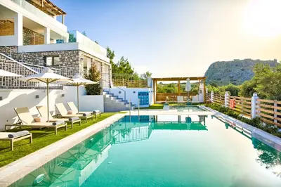 a pool with chairs and umbrellas next to a building at KOUROS STONE SUITES in Haraki