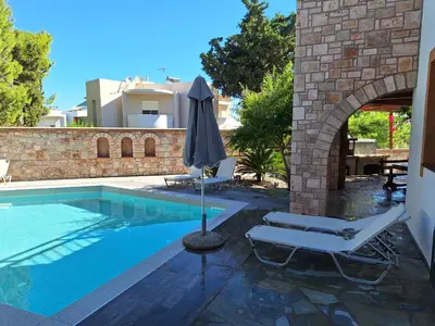 a swimming pool with two lounge chairs and an umbrella at Glamorous Villa Nefeli in Koskinou