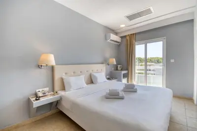 a white bedroom with a large white bed and a window at Astron Hotel Rhodes in Rhodes Town