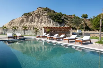 a swimming pool with lounge chairs and a mountain at Waves of Blue in Koskinou