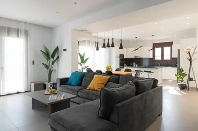 a living room with a gray couch and a kitchen at Waves of Blue in Koskinou