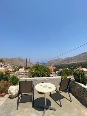 a table and two chairs on a patio with mountains in the background at ALEMINAS House 1 in Symi