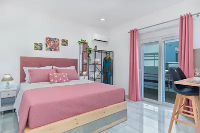a bedroom with a pink bed and a balcony at House of Helios in Pastida