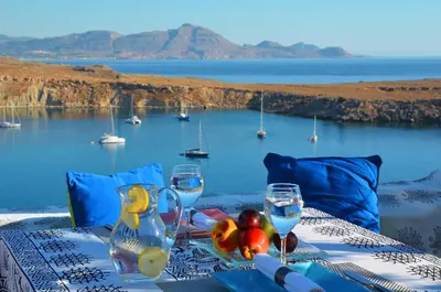 a table with wine glasses and a view of the water at Villa Melenos Lindos in Líndos