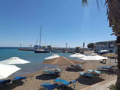 a beach with chairs and umbrellas and the ocean at Restaurant Maria Suites SunSet in Faliraki