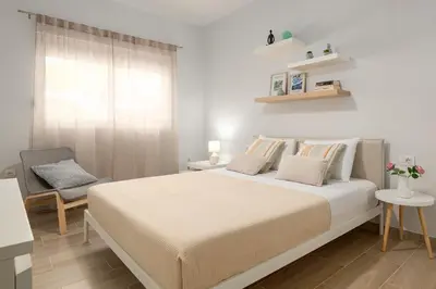 a white bedroom with a bed and a chair at Klinon Asti city apartment in Rhodes Town