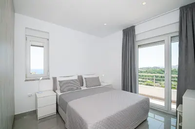 a white bedroom with a bed and a large window at Agnanti Sea View Villa in Koskinou