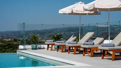 a pool with lounge chairs and umbrellas next to a swimming pool at Agnanti Sea View Villa in Koskinou
