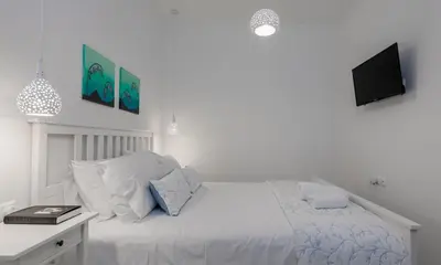 a white bedroom with a bed and a tv on the wall at Bluebell House Halki in Halki