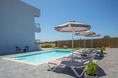 a swimming pool with chairs and umbrellas next to a pool at Captain Chris Villa in Afantou
