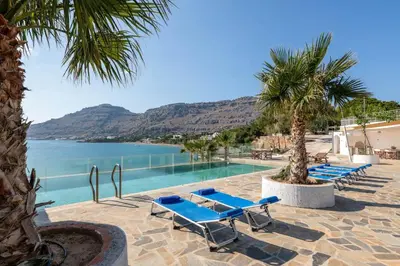 a row of blue lounge chairs next to a swimming pool at Arte Pefki Beachfront Suites in Pefki Rhodes