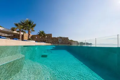 a swimming pool with blue water and palm trees at Arte Pefki Beachfront Suites in Pefki Rhodes