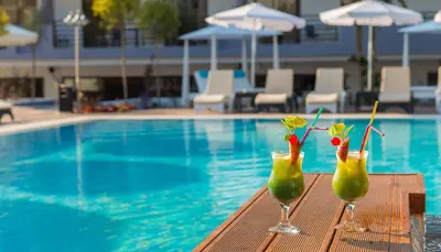 two cocktails sitting on a table next to a swimming pool at Sunny Days Hotel in Ixia