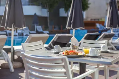 a table with a plate of food on it next to a pool at Sunny Days Hotel in Ixia