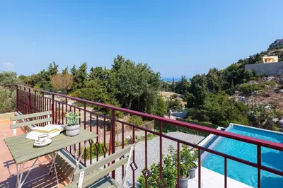 a balcony with a table and a swimming pool at Cicada Villa in Koskinou