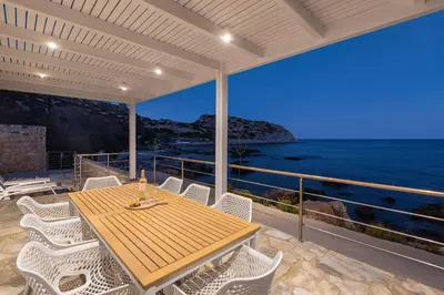 a wooden table and chairs on a balcony with the ocean at Hamilton Sea Front Villa in Archangelos