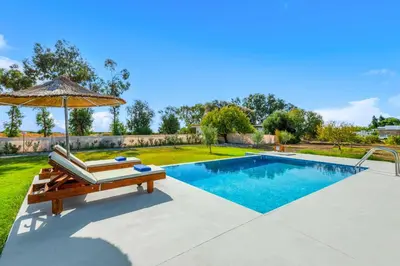 a swimming pool with a bench and an umbrella at Kalimera Villa By the Sea in Gennadi