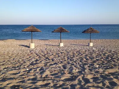 three straw umbrellas on a sandy beach near the ocean at Private beach villa Princess in Kiotari