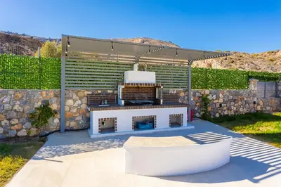 a backyard with a grill and a stone wall at Villa Livis 2 in Kiotari