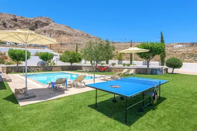 a ping pong table in the grass next to a pool at Villa Ariadne Lindos in Pefki Rhodes
