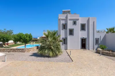 a white house with a palm tree in front of a pool at Villa Ariadne Lindos in Pefki Rhodes