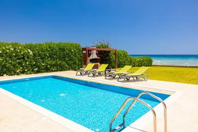 a swimming pool with chairs and a table and the ocean at Villa Metis in Lachania