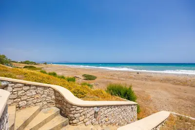 a bench on a stone wall next to a beach at Villa Metis in Lachania