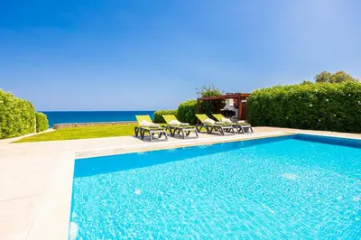 a swimming pool with chairs and the ocean in the background at Villa Tsampikos in Lachania