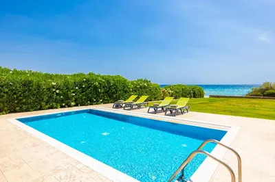 a swimming pool with chairs and the ocean in the background at Villa Dionysos in Lachania