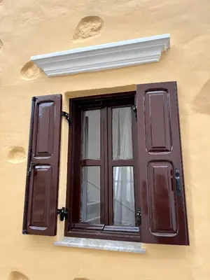 a window on the side of a building with brown shutters at Pavlos House in Symi