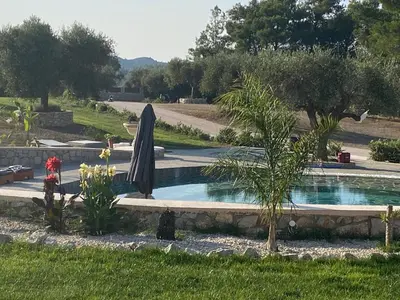 a swimming pool with an umbrella in a garden at AGROTOPIA Guesthouses in Theologos