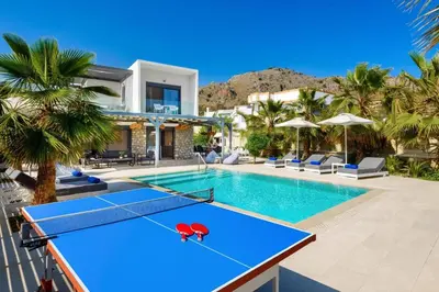 a pool with a ping pong table in front of a house at Villa Apollon Lindian Palm by Villa Plus in Kiotari