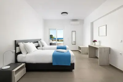 a white bedroom with two beds and a desk at Villa Zoe Blu in Kalathos