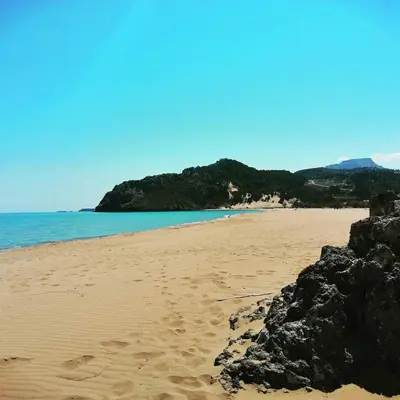 a beach with sand and the ocean and mountains at Summer holidays in Kolimbia