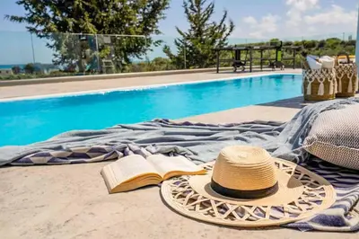 a hat and a book next to a swimming pool at Villa Anthos Kerasia in Gennadi