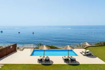 a swimming pool with chairs and umbrellas and the ocean at Paradise Beach II in Kiotari