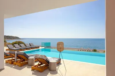 a pool with chairs and the ocean in the background at Villa Seven in Lachania