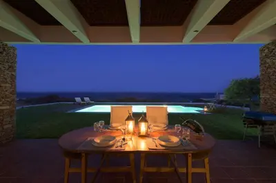a table with plates and wine glasses and a blue light at Cristelia seafront & pool villa in Lachania