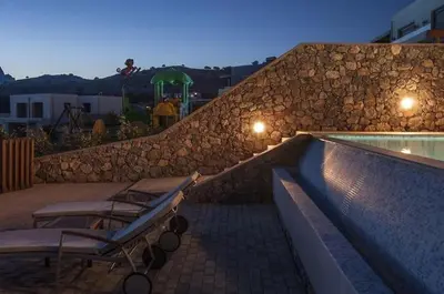 a swimming pool with chairs and a stone wall at Pefkos Heights Private Pool Villa in Pefki Rhodes