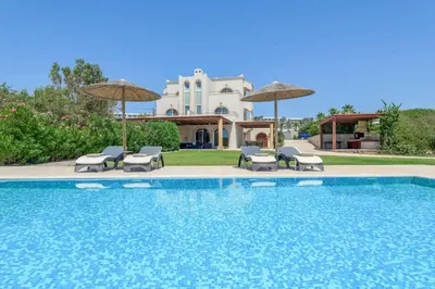 a pool with chairs and umbrellas in front of a house at Paradise Beach I in Kiotari