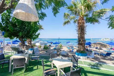 a beach with chairs tables and umbrellas and the ocean at Lido Star in Faliraki