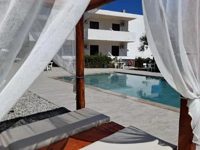 a swimming pool next to a house with a white curtain at Hotel Narkissos in Archangelos